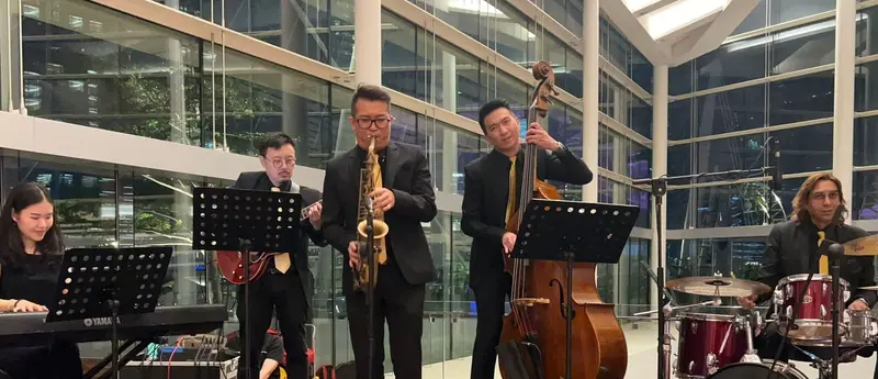 Jazz band in black suits with a saxophonist, double bass player, guitarist, keyboard player and drummer playing at an evening event